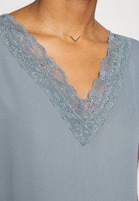 Blusa cinza com decote em V em renda, textura suave e detalhes delicados em renda ao longo da gola. Design simples e elegante.