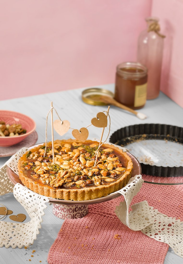 Nusstorte in einem dekorativen Keramikgeschirr, belegt mit Nüssen; herzförmige Verzierungen; beiger Boden; strukturierte Spitzenunterlage; rosa Hintergrund.