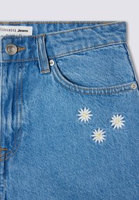 Jeans in denim blu con una texture sbiadita, caratterizzati da tre margherite ricamate in bianco e cuciture arancioni sulle tasche e sulla vita.