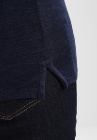 Mörkblå bomull t-shirt med sidofsiktig fåll, med en strukturerad yta och mjukt tyg, kombinerad med mörka denimjeans.