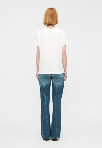 Άσπρο μπλουζάκι με κοντό μανίκι συνδυασμένο με ανοιχτό μπλε ψηλόμεσα καμπανέ τζιν παντελόνια με σχισμή στο κάτω μέρος. Ομαλή υφή.