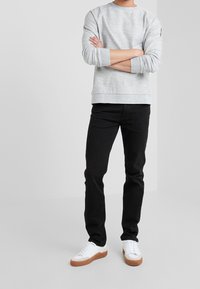 Šedá mikina s kulatým výstřihem a žebrovanými manžetami a spodním lemem, kombinovaná s černými slim fit džíny a bílými teniskami s hnědými akcenty.