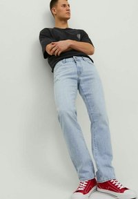 Jeans rectos de color azul claro con textura desgastada, combinados con una camiseta negra y zapatillas de lona rojas con cordones blancos y suelas de goma.