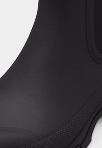 Κοντινή εικόνα μιας μαύρης λαστιχένιας μπότες με υφή στη σόλα και λείο πάνω μέρος.