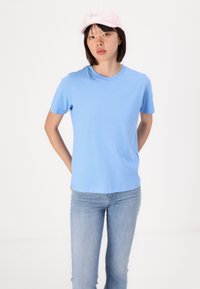 Light blue cotton t-shirt with a round neckline and short sleeves, paired with light blue denim jeans. A pink cap is worn tilted on the head.
