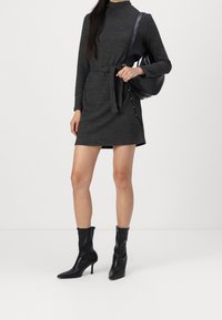 Graues langärmliges Kleid mit einem Gürtel, weicher Struktur. Kombiniert mit schwarzen Knöchelstiefeln und einer schwarzen Tasche, die eine elegante, figurbetonte Silhouette zeigt.