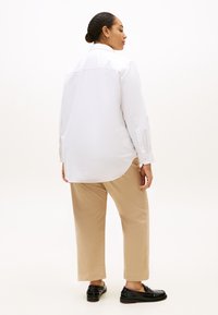 Λευκό πουκάμισο με μακριά μανίκια και καμπυλωτό κάτω μέρος, συνδυασμένο με μπεζ παντελόνι με ευθεία γραμμή και μαύρα μοκασίνια. Απλός σχεδιασμός, βαμβακερό υλικό.