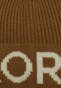 Brown knitted beanie with textured ribbing, featuring a large white lettering pattern integrated into the fabric.