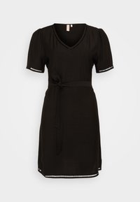 Musta mekko lyhyillä puffihihnoilla, V-pääntiellä ja nauhavyöllä. Sisältää pieniä valkoisia yksityiskohtia hihansuiden ja alaosan reunoissa. Silkkinen rakenne.