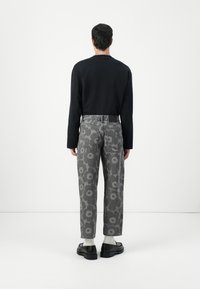 Jeans grigi con motivo floreale, con taglio dritto e vita alta. Abbinati a una camicia nera a maniche lunghe e scarpe nere.