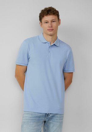 Hellblaues Poloshirt aus Baumwolle, mit Kragen, Drei-Knopf-Leiste und kurzen Ärmeln. Getragen mit hellblauen Jeans.