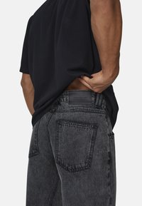 Jeans in denim grigio scuro con una finitura sbiadita, con tasche posteriori e un'etichetta in pelle sulla vita, abbinati a una maglietta nera.