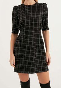 Schwarzes Kurzarmkleid mit einem weißen Rautenmuster, figurbetonter Silhouette, rundem Ausschnitt und strukturiertem Stoff.