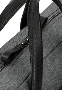 Manici in pelle nera attaccati a una borsa di tessuto grigio texturizzato con una cerniera argento e un dettaglio in pelle per la cerniera.