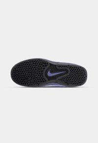 Semelle de chaussure avec motif alvéolé noir et célèbre swoosh Nike violet au centre sur fond gris.