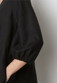 Czarna lniana bluzka z dekoltem w kształcie V i bufiastymi rękawami. Charakteryzuje się teksturowanym materiałem, luźnym krojem i widocznymi szwami.