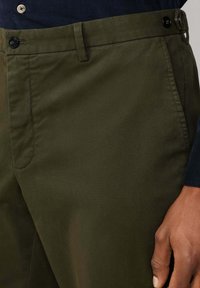 Olijfgroene corduroy pantalon met een rechte pijp, voorzien van een knoopsluiting en voorkruiden. Gladde textuur met verticale ribbels.