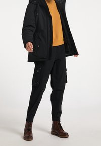 Giacca imbottita nera con cappuccio, abbinata a un maglione senape e pantaloni cargo neri con tasche. Completato con stivali marroni stringati.