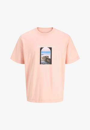 Garçon aux cheveux bouclés portant une veste bleu clair par-dessus un t-shirt rose graphique, un short couleur crème, des chaussettes blanches et des chaussures beiges, debout sur fond blanc.