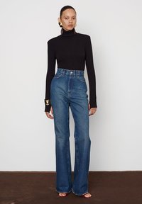 Čierny rolák skombinovaný s džínsy s vysokým pásom v modrom flare strihu. Model má na sebe zlaté výnimočné náušnice; minimalistický, čistý dizajn.