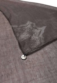 Un tissu léger gris avec un motif de montagne subtil, bordé d'une fine couture, présente un emblème argenté à la base fixé par une ficelle.