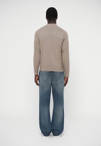 Béžový pletený sveter s dlhými rukávmi a okrúhlym výstrihom, kombinovaný s voľnými modrými rifľami s vyblednutým efektom a zadnými vreckami.