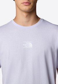 Jasnofioletowy bawełniany T-shirt z okrągłym dekoltem i krótkimi rękawami. Na piersi znajduje się biały logo w prostokątnym obrysie.