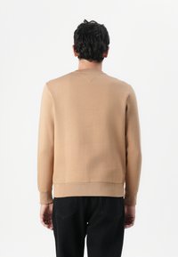 Beige sweatshirt lavet af blødt materiale, med lange ærmer, rund halsudskæring og ribbede manchetter, båret med mørkeblå jeans.