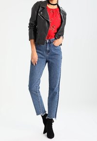 Giubbotto da motociclista in pelle nera, blusa rossa a fiori, jeans blu a vita alta con orli sfilacciati, abbinati a stivaletti neri. Design semplice.
