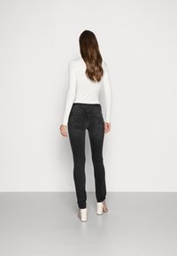 Svarta smala jeans med hög midja, med två bakfickor och en slät yta, kombinerat med en vit ribbad långärmad topp.