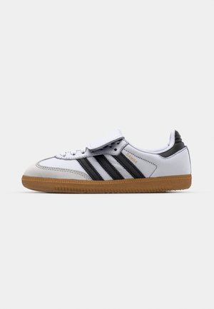 Hvide lædersneakers med sorte striber og grå detaljer, der har en rund tå og en sål i gummi. Velcro-lukning og snørelukning.