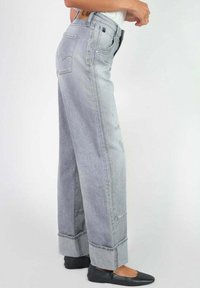 Jean large gris clair à taille haute, en tissu denim, avec des ourlets retroussés et un accent de marque discret sur la poche arrière.