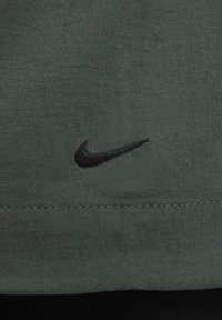 Tejido verde oscuro con una textura suave; presenta un logo de Nike bordado en negro en la parte delantera cerca del dobladillo.