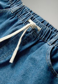 Niebieskie szorty dżinsowe z elastycznym paskiem i białym sznurkiem. Posiadają widoczne szwy i miękką, teksturowaną tkaninę.