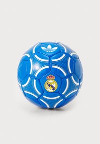 Modrá futbalová lopta s textúrovaným povrchom, bielymi akcentmi, logom Adidas a emblémom Real Madrid s korunou. Dizajn s hexagónovými panelmi.