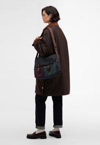 Mala mensageiro em cores escuras com seções em verde, azul e borgonha. Apresenta alças ajustáveis, duas fivelas e uma aba texturizada.