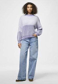 Pleteni pulover s gradijentnim prugama u lavandi i bijeloj boji, opuštenog kroja, rebraste teksture; kombiniran s trapericama visokog struka širokih nogavica u plavoj boji.