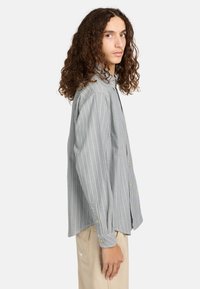 Stribet skjorte i grå og hvid, med lange ærmer, guldknapper og en afslappet pasform. Bæres med beige bukser.