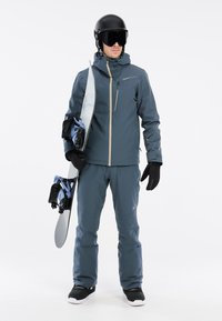 Snowboardoutfit in donkerblauw waterdicht materiaal, met een jack met rits, bijpassende broek, zwarte handschoenen en een helm met goggles.