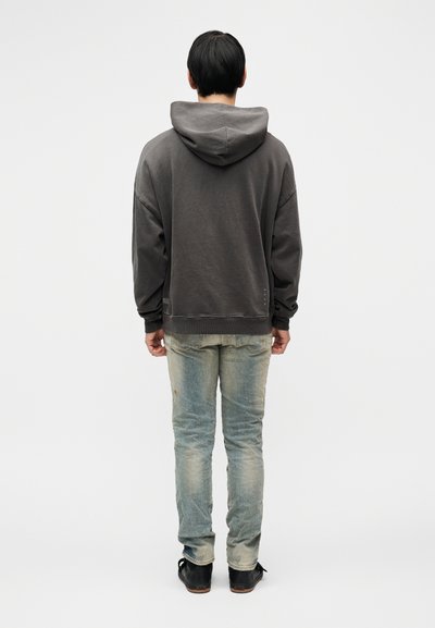 Σκούρα γκρι φούτερ με μεγάλη κουκούλα, χαλαρή εφαρμογή, ριμπ μανσέτες και τελείωμα. Φορεμένο με ξεθωριασμένο μπλε τζιν και μαύρα παπούτσια, από πίσω.