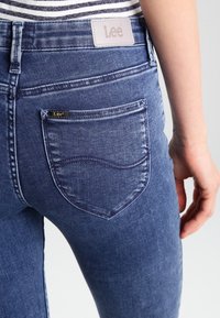 Mörkblå denimjeans med slim fit, som har en bakficka och en läderetikett vid midjan med "Lee" präglat.
