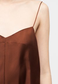 Κοντινό πλάνο ενός ατόμου που φοράει καφέ αμάνικο φόρεμα με λεπτές ράντες ώμων και εφαρμοστό μπούστο.