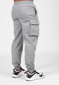 Grijze sweatpants met cargozakken, elastische tailleband en manchetten aan de enkels. Gecombineerd met zwart-witte sportschoenen.