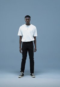 Maglietta bianca in cotone, jeans neri e sneakers alte nere. Design semplice con vestibilità comoda e accessori minimi.