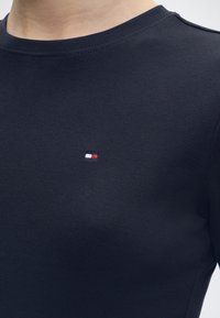 Μπλούζα σε ναυτικό μπλε με στρογγυλή λαιμόκοψη και μικρό κόκκινο, άσπρο και ναυτικό μπλε λογότυπο κεντημένο στο αριστερό στήθος.