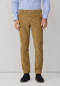 Khaki corduroy broeken met een slim fit, voorzien van een knoopsluiting en riemlussen, gecombineerd met donkerblauwe suède schoenen. Verticale textuur zichtbaar.