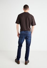 Dark brown short-sleeve shirt, blue denim jeans, and brown shoes. Jeans feature rear pockets with distinctive stitching accents.