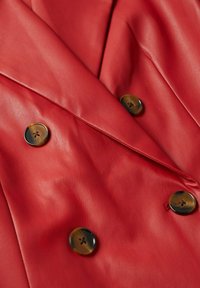 Veste en cuir rouge avec col à revers et quatre boutons ronds marron disposés en style croisé.