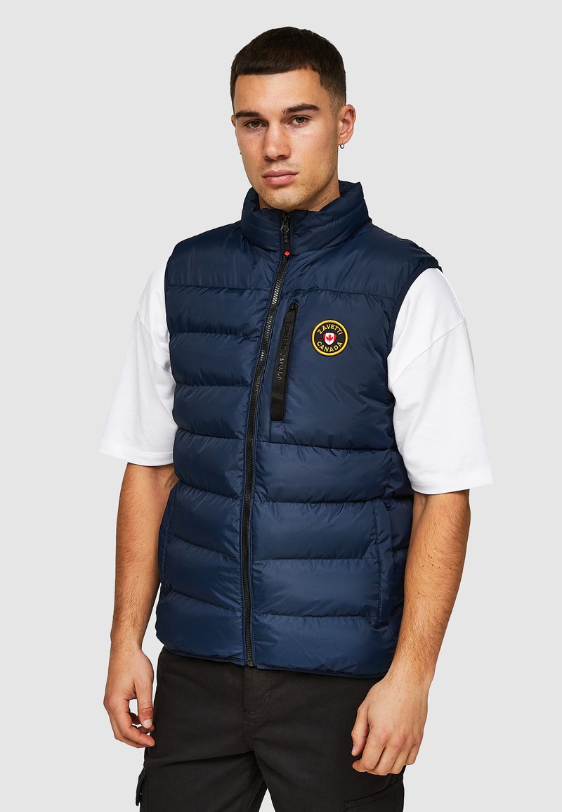 Marineblauwe puffervest met hoge kraag, voorrits en logo-opdruk. Gemaakt van glad, gewatteerd materiaal met een horizontaal gestikte stijl.