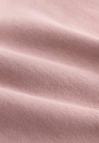 Tejido suave y texturizado en un color rosa claro, que revela un fino patrón tejido con sutiles líneas horizontales. Ideal para aplicaciones de vestimenta.